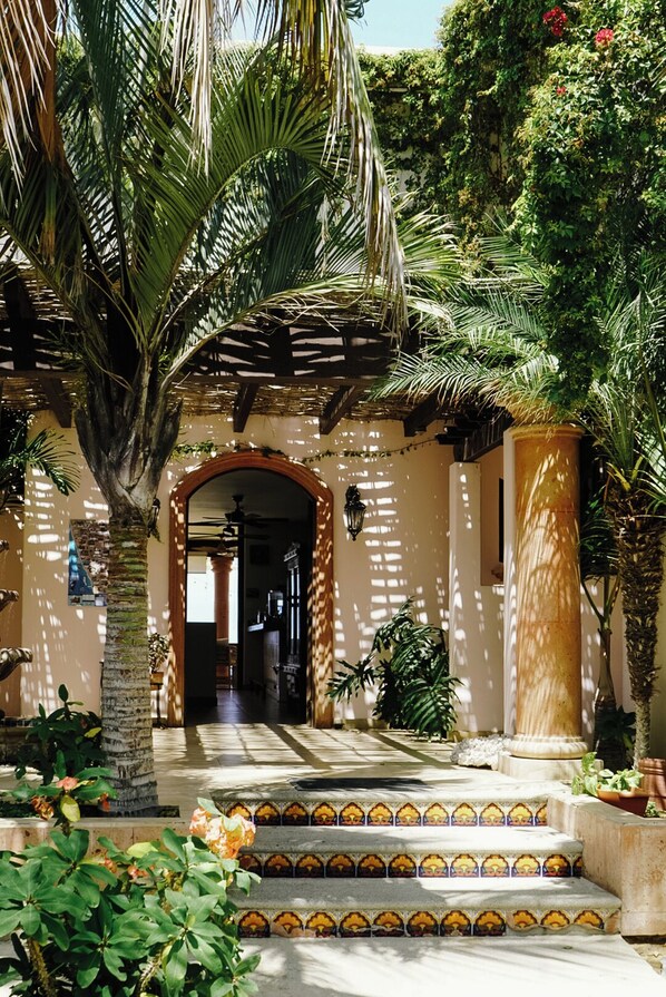 A courtyard with a palm tree, steps leading to an archway, and a tiled floor. - The Cerritos Beach Inn (El Pescadero)