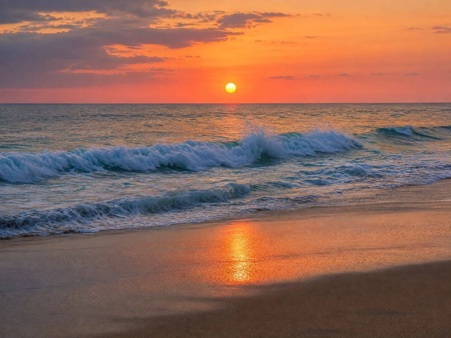 A beach with waves and a sunset.