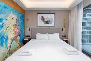 Ein Hotelzimmer mit einem großen Bett, einem Pferdegemälde, einem gerahmten abstrakten Kunstwerk und Blick auf ein Gebäude durch das Fenster.