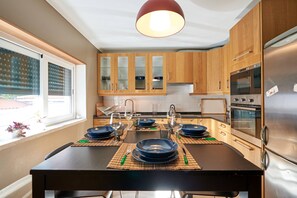 A modern kitchen with wooden cabinets, a stainless steel refrigerator, and a dining area with a black table set for four. - Exquisite Townhouse in Lisbon- Garage & Terrace (Lisboa)