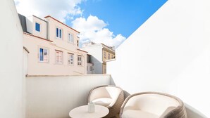 Ein Balkon mit zwei Korbstühlen und einem kleinen runden Tisch mit Blick auf benachbarte Gebäude.