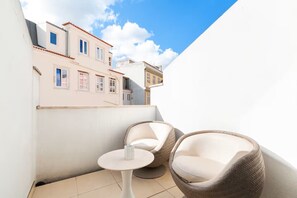 Ein Balkon mit zwei Korbstühlen und einem kleinen runden Tisch mit Blick auf benachbarte Gebäude.