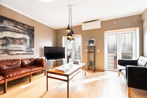 Ein modernes Wohnzimmer mit einer Ledersofa, einem Holztisch, einem Fernseher und einem großen abstrakten Gemälde.