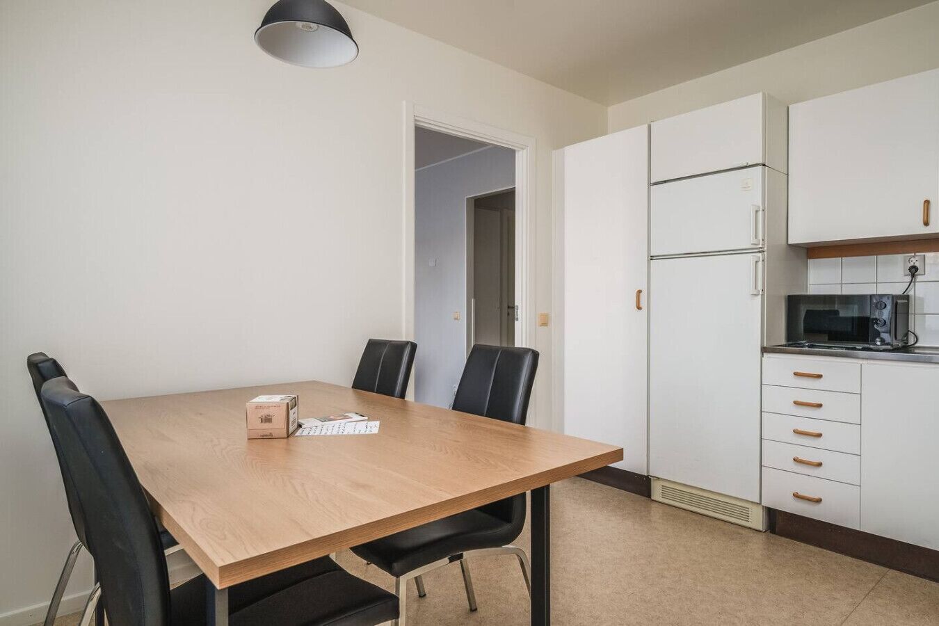 A compact kitchen with a dining table, chairs, a microwave, and a refrigerator.