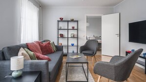 A modern living room with a grey sofa, a coffee table, a bookshelf, a grey armchair, and a TV mounted on the wall. - Bright, Modern Apartment in the Heart of Norberg (Norberg)