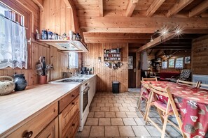 A wooden cabin interior with a kitchen, dining area, and a visible door leading to another room. - Chalet “8p Simple - La Hulotte”: Mountain View, Private Terrace & Wi-Fi (Verchaix)