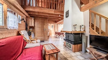 A wooden cabin interior with a sofa, a television, a fireplace, and a dining area.