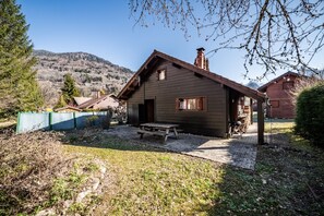 A wooden cabin with a sloped roof, a patio with a picnic table, and a view of mountains in the background. - Chalet “8p Simple - La Hulotte”: Mountain View, Private Terrace & Wi-Fi (Verchaix)
