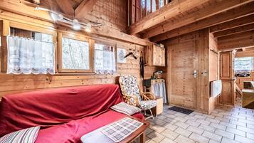 A wooden cabin interior with a red sofa, a patterned bench, a wicker chair, and a dining area.
