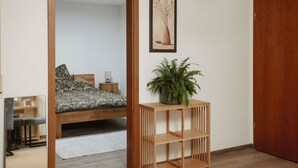 A bedroom with a wooden bed, a small bedside table, a mirror, a framed picture on the wall, and a wooden console table with a plant.