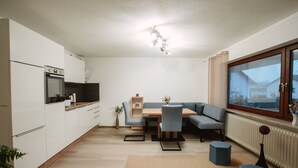 A modern kitchen with built-in appliances, a dining area with a sofa and table, and a large window.