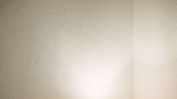 Une chambre à coucher avec une tête de lit en bois, une table de chevet ronde surmontée d’une lampe, et une couvre-lit à motifs floraux.