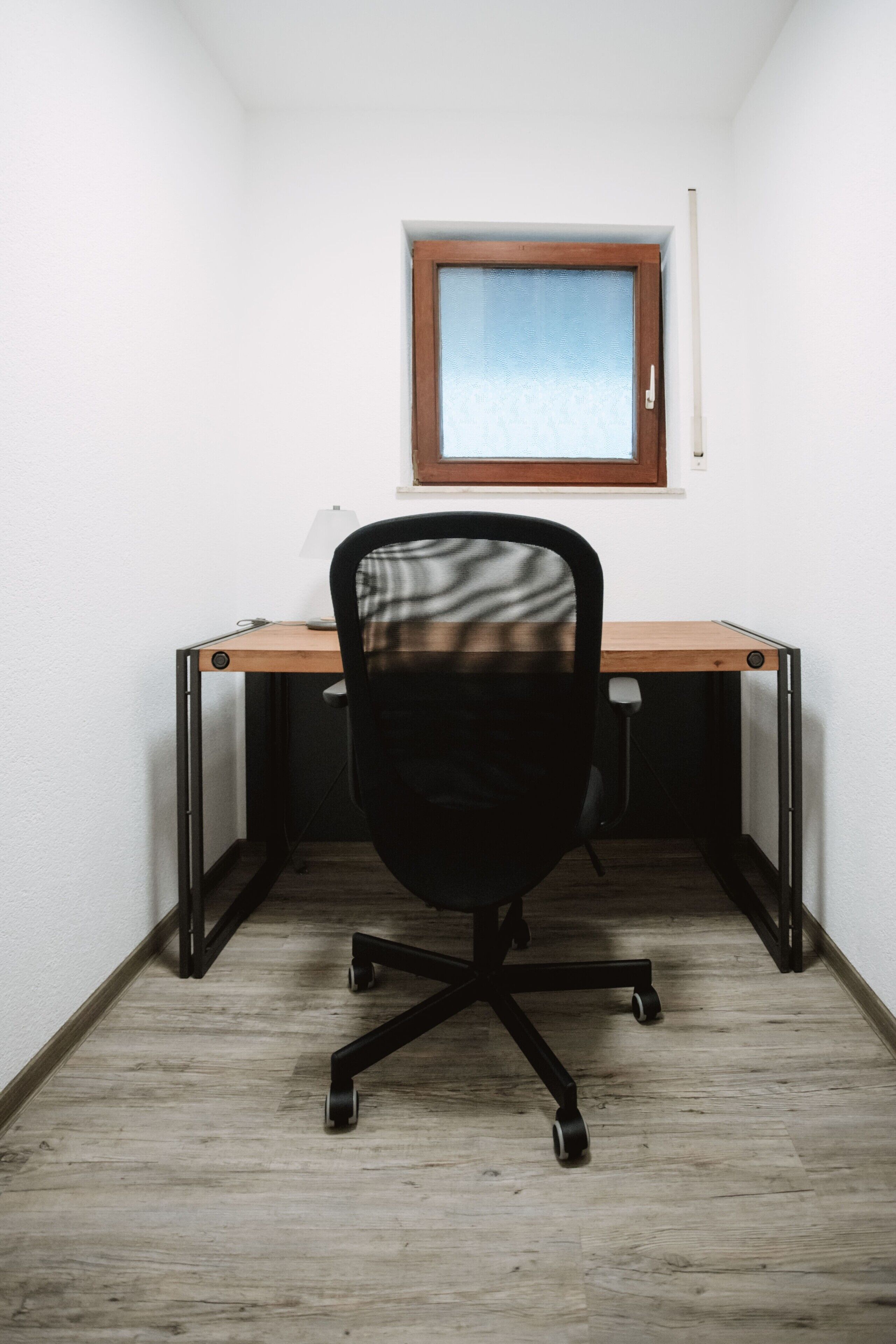 Ein kleiner Büroraum mit Schreibtisch, Stuhl und Fenster.