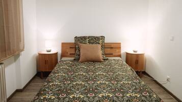 A bedroom with a wooden headboard, a floral bedspread, two bedside tables with lamps, and a wooden floor.