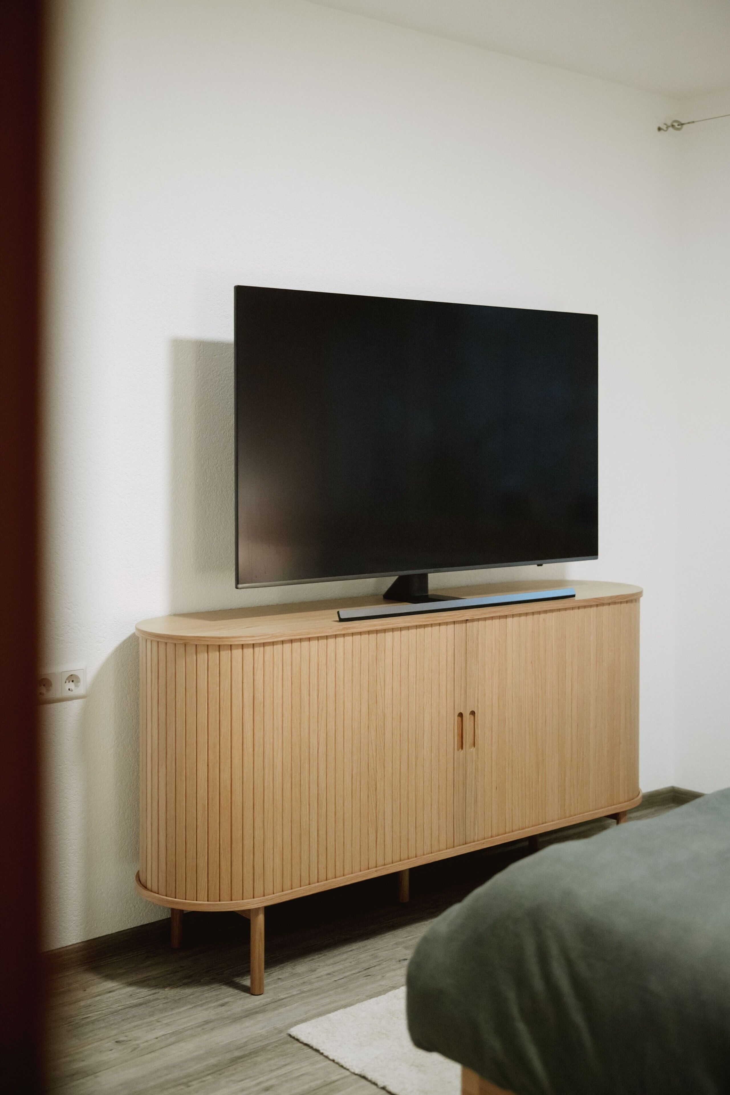A television on a wooden cabinet in a room with a bed.