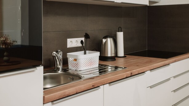 A modern kitchen with a wooden countertop, stainless steel sink, and white cabinetry.
