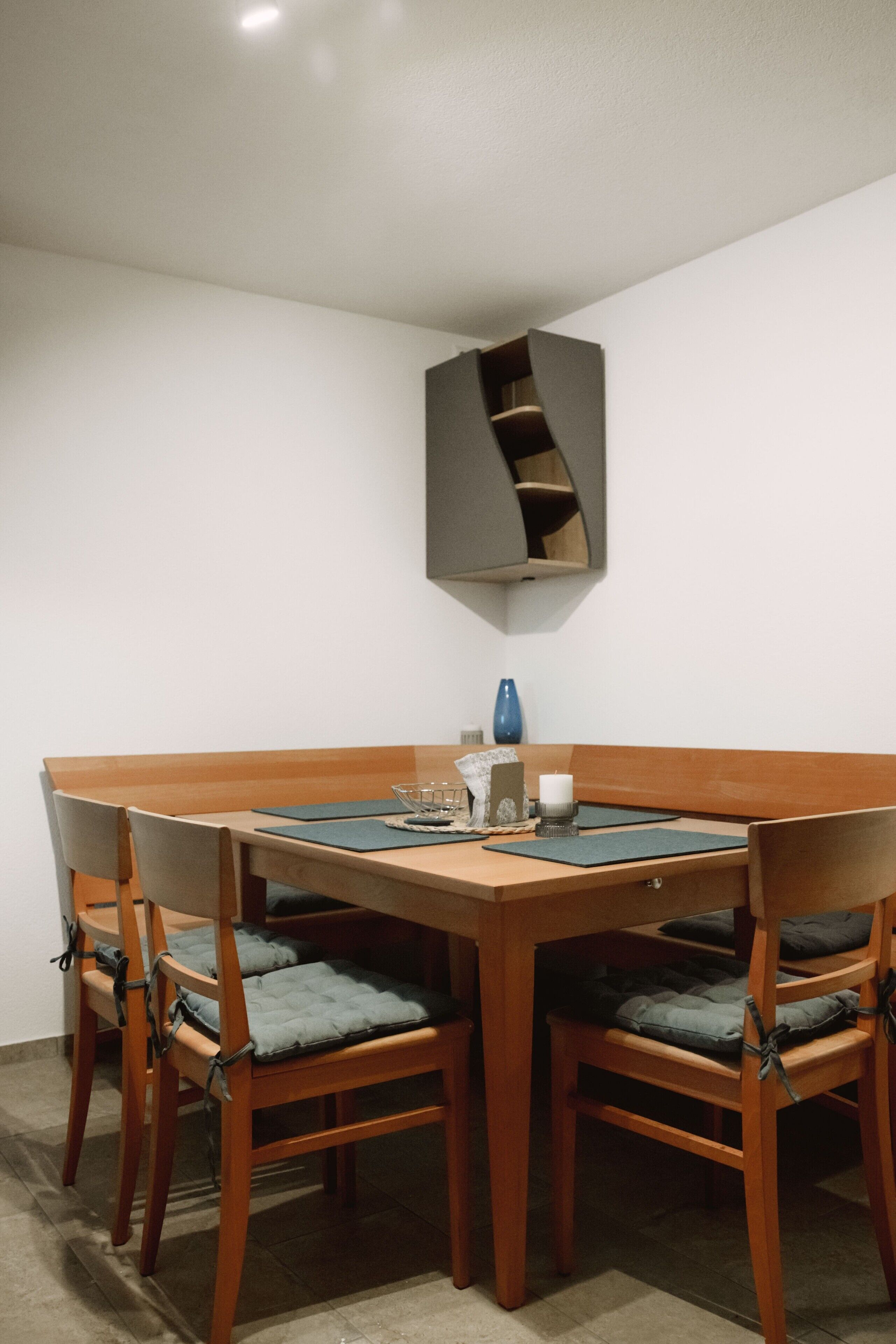 A dining area with a wooden table and chairs, a blue vase, and a wall-mounted shelf.