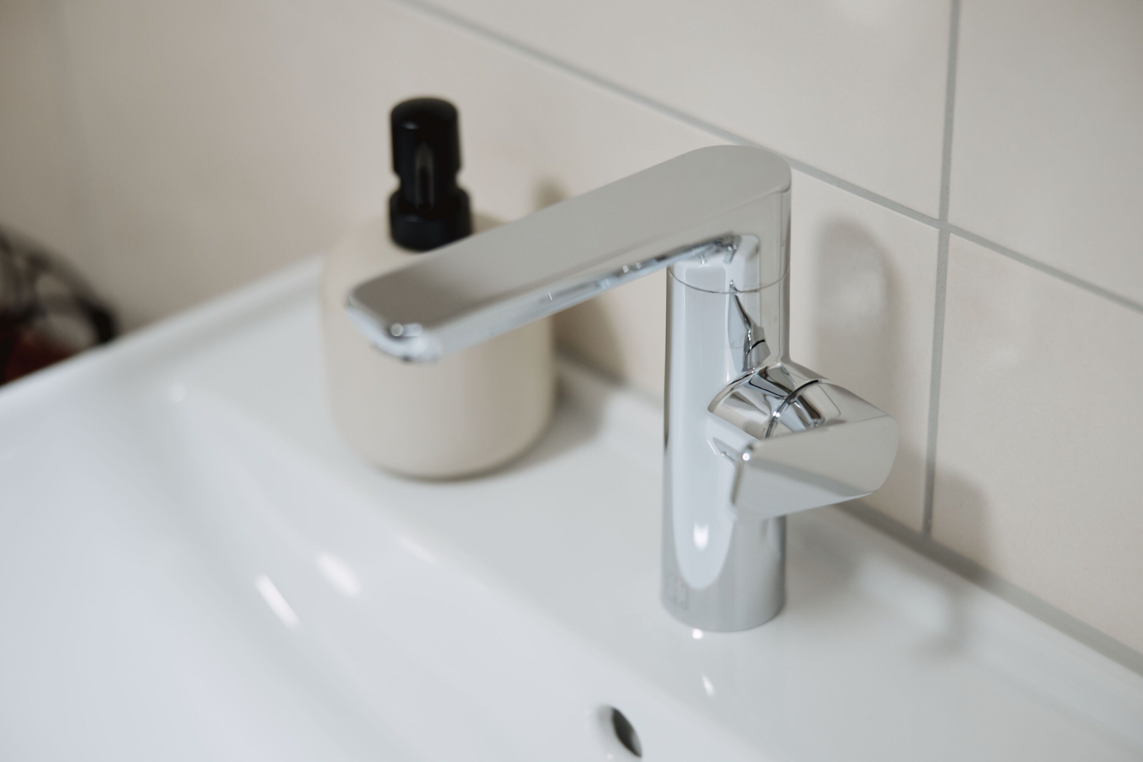 Een wastafel met een chromen kraan en een zeepdispenser.