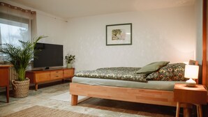 Een slaapkamer met een bed, een televisie, een plant en een lijstje aan de muur.
