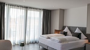 Una habitación de hotel moderna con una cama grande, cortinas grises, una mesita de noche y una lámpara.