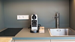 Una cocina moderna con estufa integrada, cafetera, lavamanos y un enchufe en la pared.