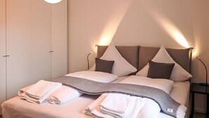 A modern bedroom with a large bed, a headboard with integrated lighting, and a bedside table with a lamp. - Munich Finest Apartments 6 by Interhome (Munich)