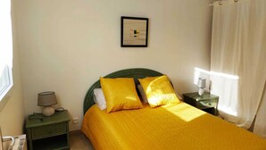 Un dormitorio con cama, mesita de noche, lámpara, un cuadro en la pared y ventana con cortinas.