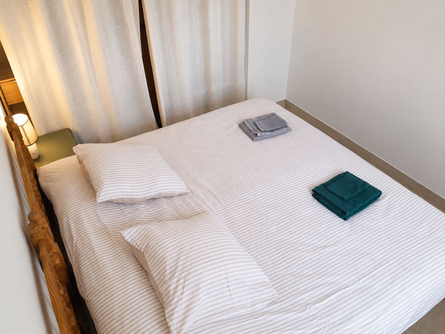 Un lit simple avec une literie blanche et deux oreillers, une serviette pliée et une couverture pliée.
