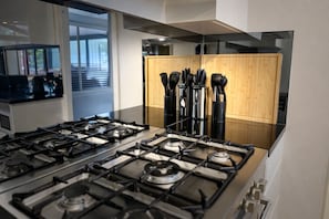 A modern kitchen with a gas stove, wooden cabinets, and a view of the outdoors. - Resort-Style Family Retreat with Pool & Views (Albion Park)