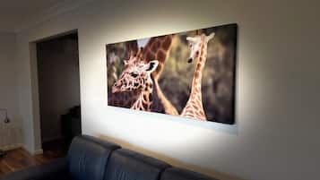 A living room with a black leather sofa and a large framed picture of giraffes on the wall.