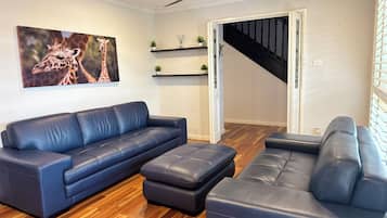 A living room with a dark blue sofa, a matching ottoman, a ceiling fan, and a staircase leading to another level.
