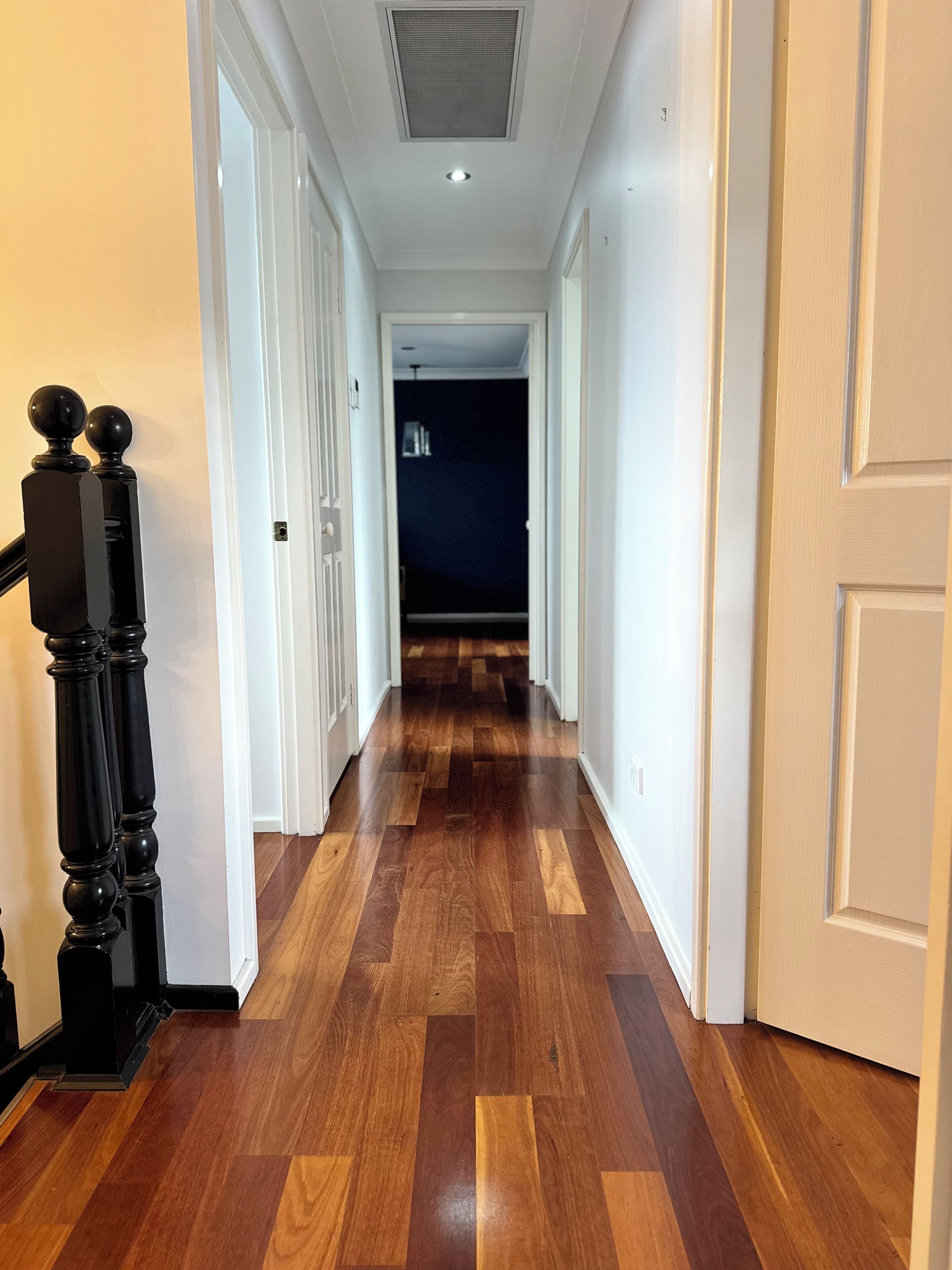 A hallway with wooden flooring, white doors, and a black balustrade.