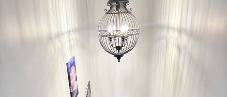 Una escalera de madera con balaustres negros, paredes blancas y un colgador de luz.