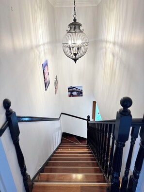 A wooden staircase with black balusters, white walls, and a hanging light fixture.
