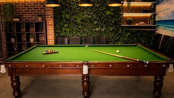 A pool table with balls, surrounded by a brick wall and a green leafy wall.