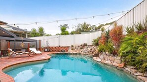 Ein Garten mit Pool, Liegestühlen und einer Steinmauer mit Bepflanzung.
