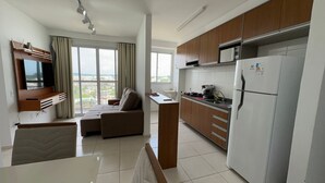 A modern apartment with a living area, kitchenette, and a large window offering a city view. - Apto. Novo Perto da Praia da Ponta Negra (Manaus)