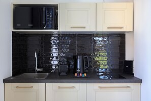 A kitchen with a black tiled backsplash, a microwave, a coffee maker, and a sink. - Helvetia 24 (Baveno)