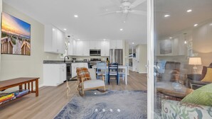 A modern kitchen with white cabinets, a microwave, and a refrigerator. There is a dining area with a table and chairs. - Haney's B By The Sea - Unit B of Triplex (Pawleys Island)