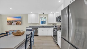 A modern kitchen with white cabinets, a stainless steel refrigerator, and a dining area with a table and chairs. - Haney's B By The Sea - Unit B of Triplex (Pawleys Island)