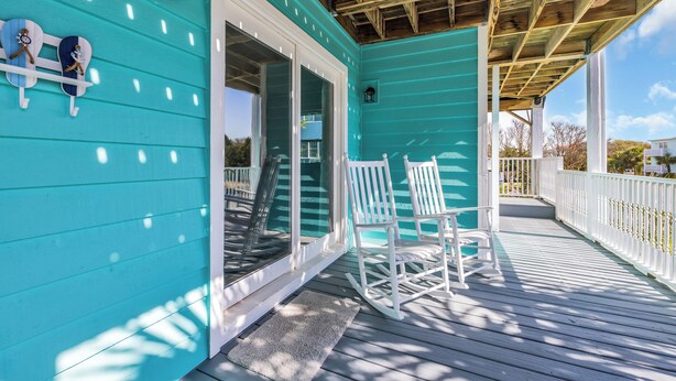 A turquoise wooden deck with white railings, a covered area with a wooden ceiling, and two white rocking chairs. - Haney's By The C - Unit C of Triplex (Pawleys Island)