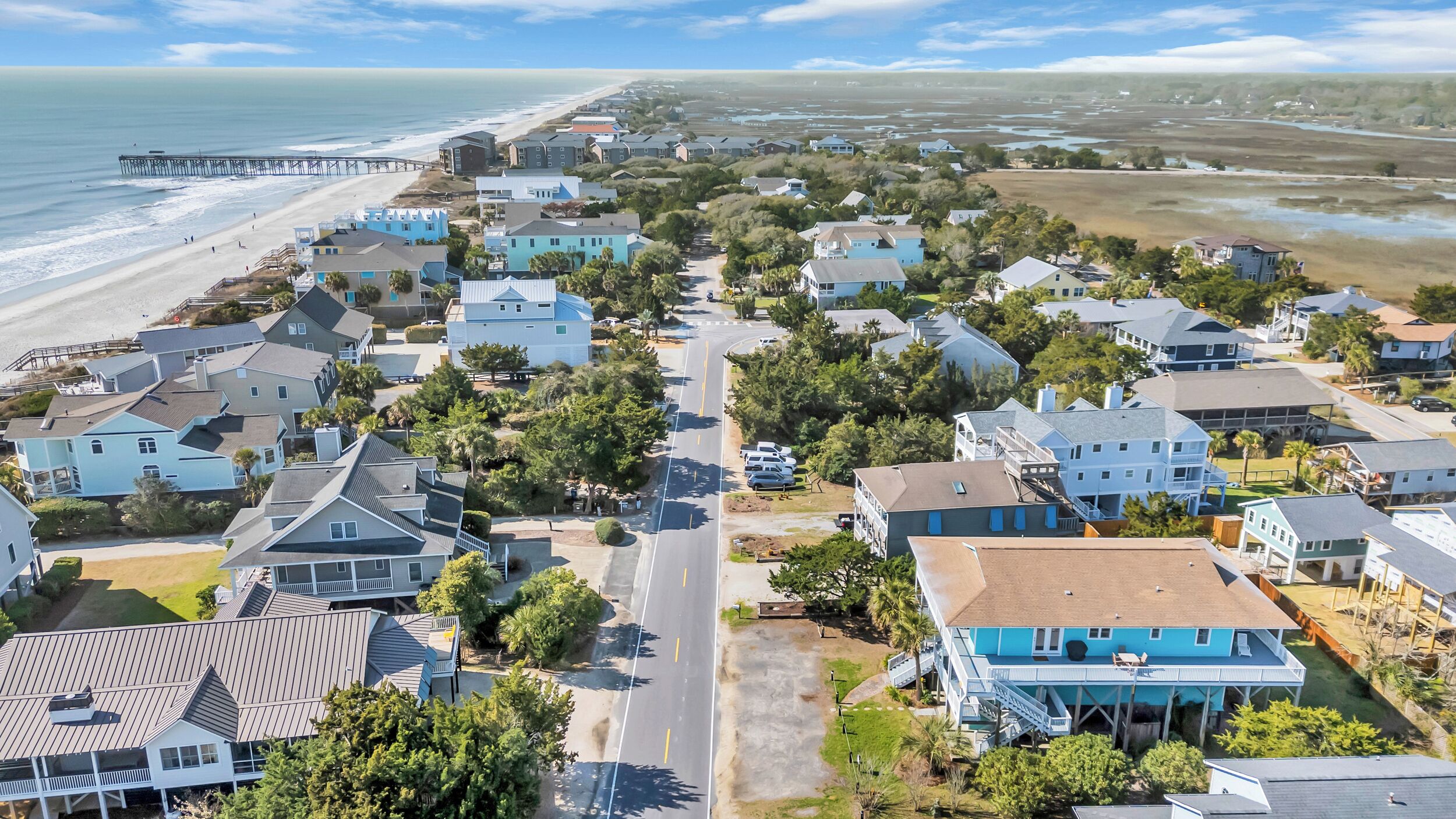 An aerial view of a coastal residential area with houses, a beach, and a pier.