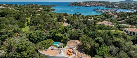 Um imóvel à beira-mar com piscina, cercado por vegetação exuberante e vista para o mar com barcos.