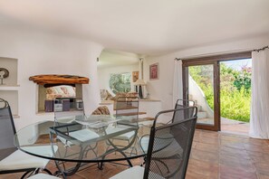 A dining area with a glass table and chairs, a wooden beam above the seating, and a view of a garden through a glass door. - Villa Abbaiola - Porto Cervo Marina (Porto Cervo)
