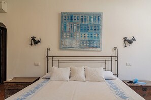 Ein Schlafzimmer mit einem Bettgestell aus Metall, einer gemusterten Bettdecke und einem an der Wand hängenden Kunstwerk.