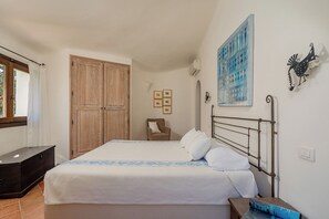 A bedroom with a bed, a wardrobe, a chair, and a wall-mounted artwork. - Villa Abbaiola - Marina Porto Cervo (Porto Cervo)
