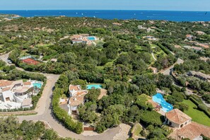 An aerial view of a residential area with multiple houses, a winding road, and a large body of water in the background. - Villa Abbaiola - Porto Cervo Marina (Porto Cervo)