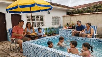 Un espace autour d’une piscine, avec des murs recouverts de carreaux, une table avec des boissons, et des personnes assises ou debout.