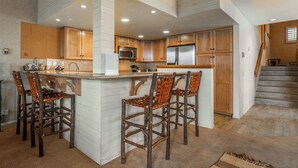 Una cocina amplia con una isla central, taburetes de madera y un refrigerador de acero inoxidable.