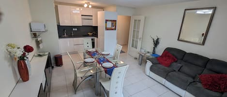 Una sala de estar moderna con comedor, un sofá gris y una cocina al fondo.
